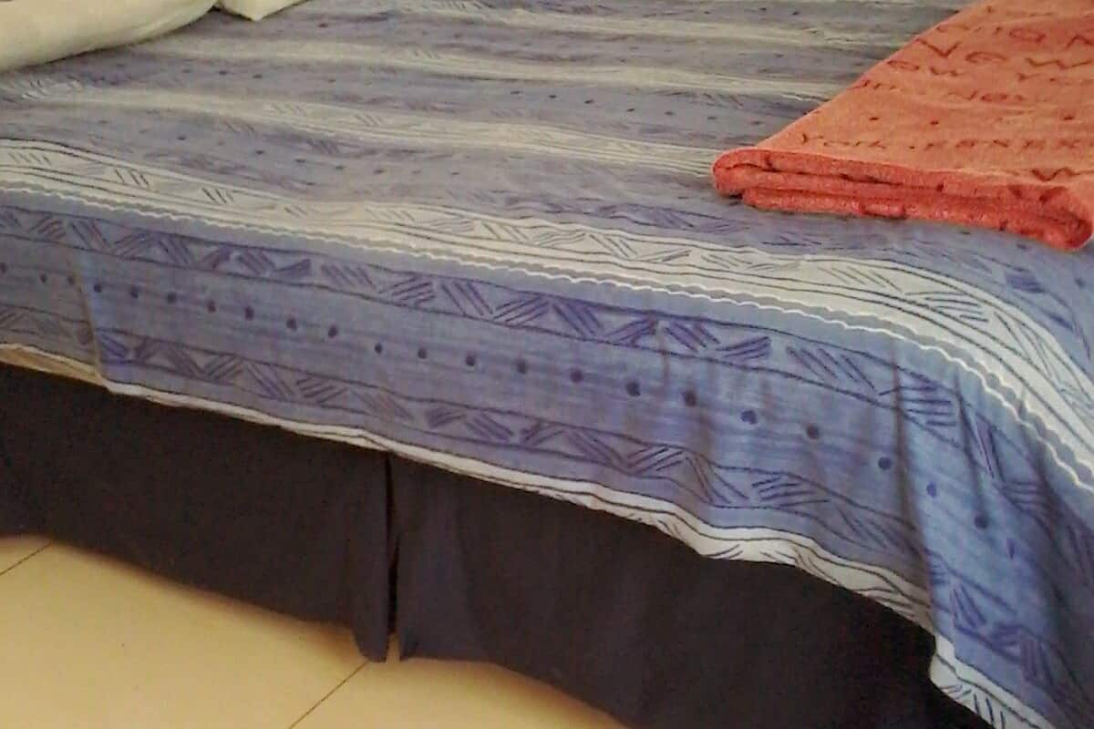 Una cama con una colcha estampada y una manta roja.