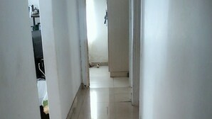 Un estrecho pasillo con baldosas, paredes blancas y una puerta visible al final.