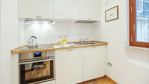 A compact kitchen with white cabinets, a stainless steel oven, a sink, and a window with a view. - Bufalo - WR Apartments (Rome)