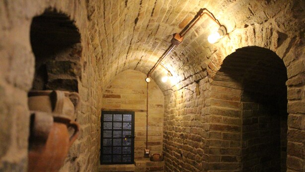 A narrow stone corridor with arched doorways, a window with bars, and hanging light fixtures. - B&B Porta Santa Lucia (Fermo)