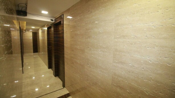 A hallway with a polished floor, a wooden door, and a textured wall. - Hotel Alfa International (Mumbai)