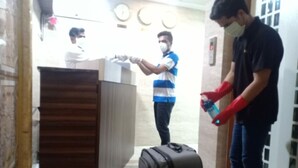 A reception area with a wooden desk, a black suitcase, and a person wearing red gloves. - Hotel Alfa International (Mumbai)