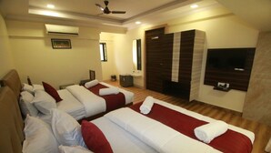 A hotel room with two beds, a TV, a ceiling fan, and a wooden floor. - Hotel Alfa International (Mumbai)