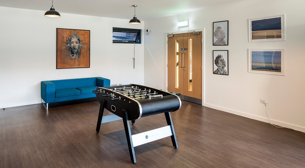 Une pièce avec une table de baby-foot, un canapé bleu et des œuvres d’art accrochées aux murs.