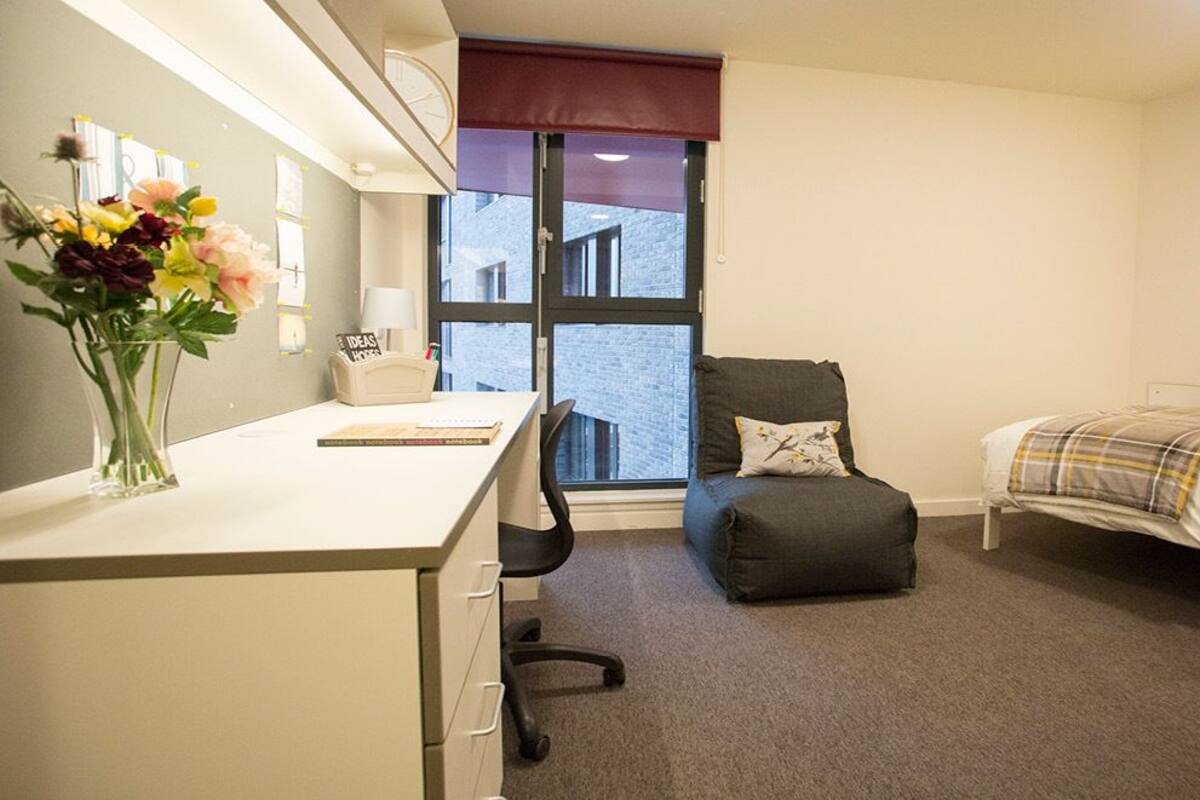 A compact hotel room with a desk, chair, bed, and a window with a view of the outside.