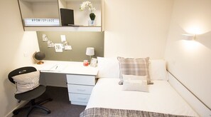 A compact hotel room with a single bed, a desk with a chair, a small desk lamp, a globe, and a bulletin board with notes. - Powis Place - Campus Residence (Aberdeen)
