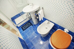 Et badeværelse med blå fliser på gulvet, en hvid vask, en bidet og en træsæde til toilettet.