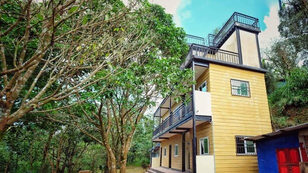 A two-story building with a balcony, surrounded by dense greenery.