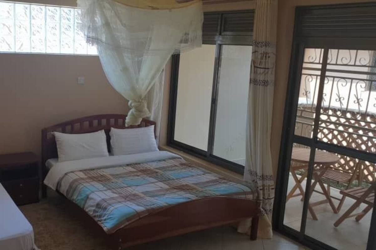 Ein Schlafzimmer mit zwei Einzelbetten, einem Holz-Kopfteil, einem Fenster mit Moskitonetz und einem Balkon mit Holzgeländer.
