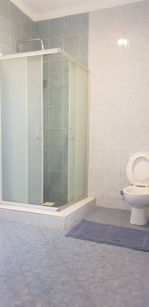 Un baño con ducha envuelta en vidrio, inodoro y un tapete azul en el suelo.