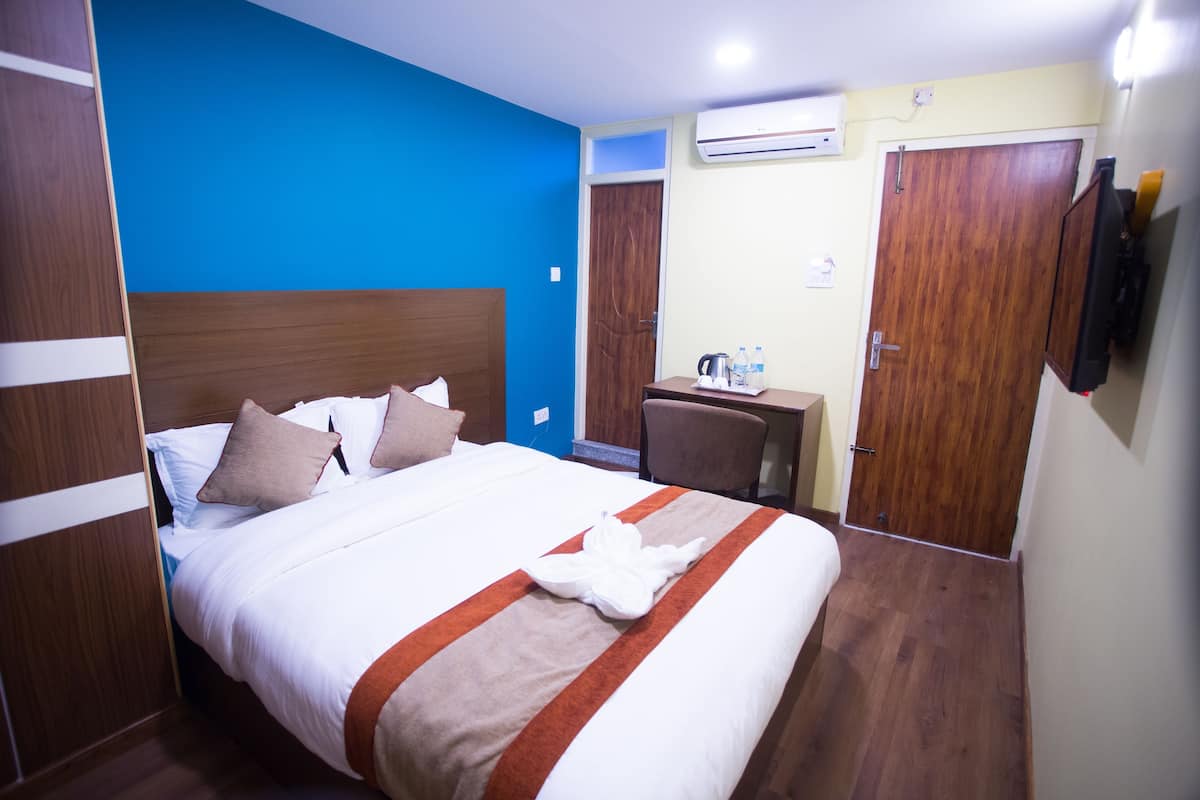 A hotel room with a large bed, a desk, a chair, an air conditioning unit, and a television.