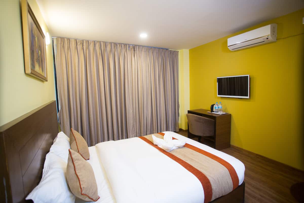 A hotel room with a bed, a desk, an air conditioner, and a television.