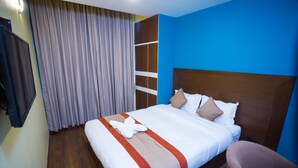 A hotel room with a large bed, a wooden wardrobe, a chair, and a curtain. - Hotel Rosemary Homes (Kathmandu)