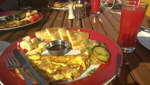 A breakfast plate with eggs, toast, potatoes, and fruit, along with condiments and a glass of red drink. - Hotel Rosemary Homes (Kathmandu)