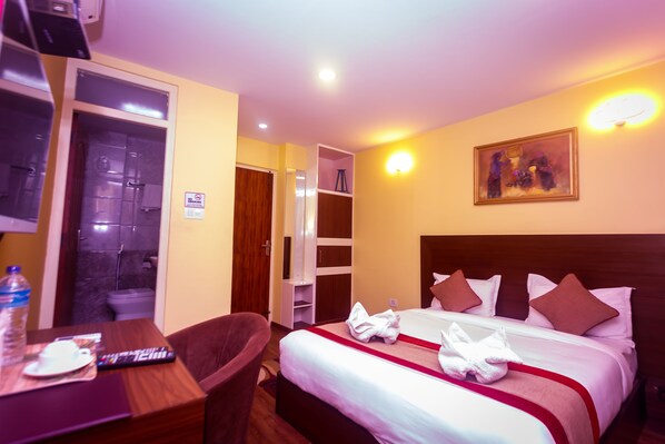 A hotel room with a bed, bedside table, chair, and a shower area.