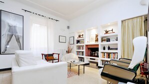 Un salon moderne avec un canapé blanc, une table basse, un fauteuil de lecture et une bibliothèque remplie de livres et d’objets décoratifs.