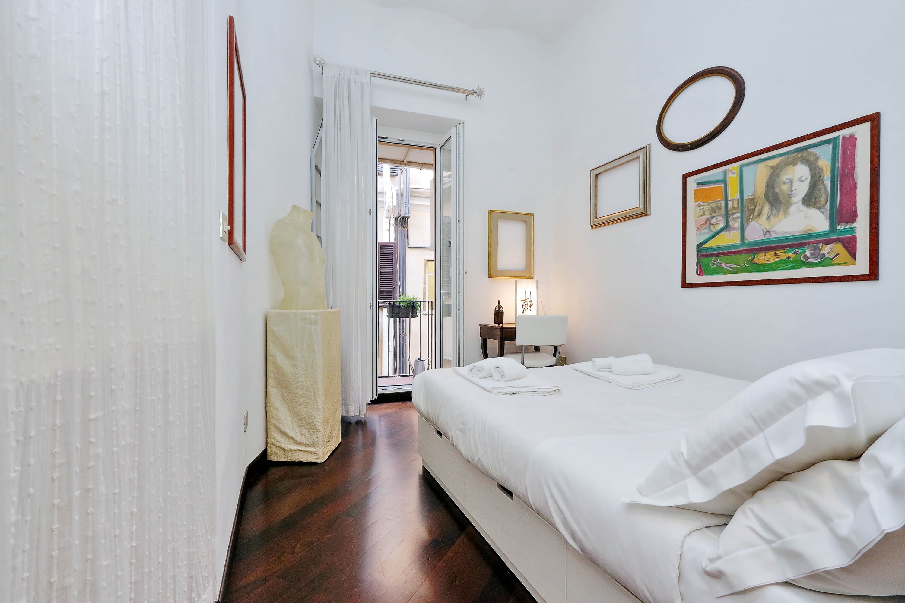 Une chambre d’hôtel avec un lit, une table de chevet, une fenêtre avec des rideaux et des œuvres d’art accrochées au mur.