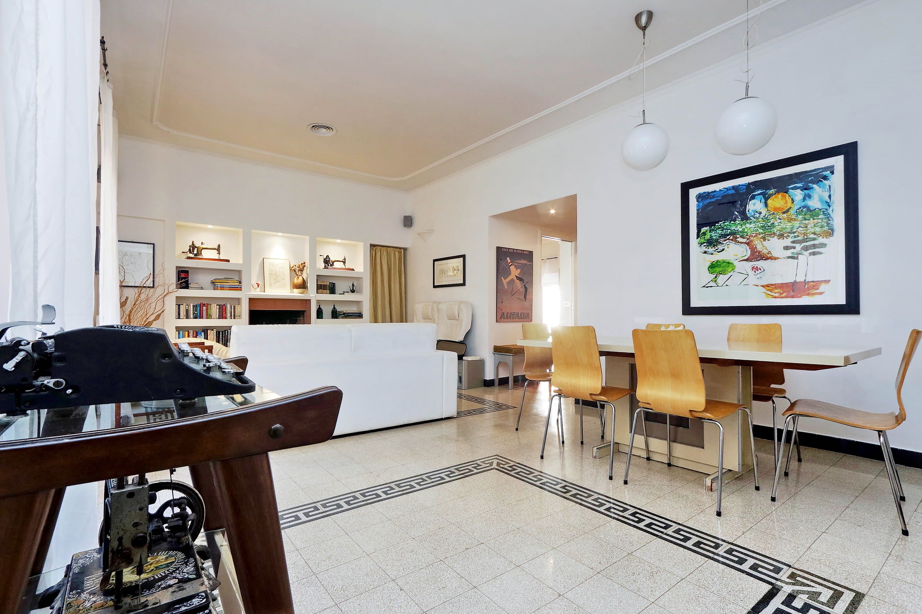 Una sala moderna con un sofá blanco, una mesa de comedor con sillas y una zona de cocina al fondo.