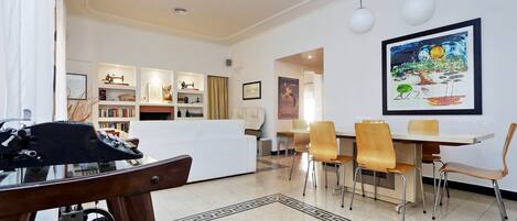 Una sala moderna con un sofá blanco, una mesa de comedor con sillas y una zona de cocina al fondo.