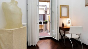 Une pièce avec un plancher en bois, une chaise blanche, un bureau avec une lampe et une grande sculpture.