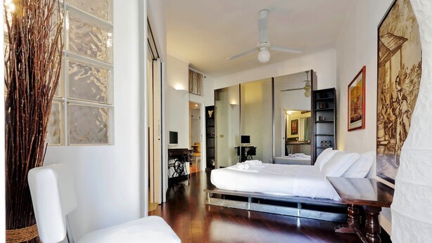 Une chambre d’hôtel équipée d’un lit, d’une chaise, d’un bureau, d’un miroir et d’un ventilateur de plafond.