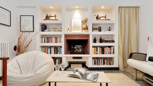 Un salon avec une cheminée, des étagères à livres, un fauteuil en forme de poire et une table basse.