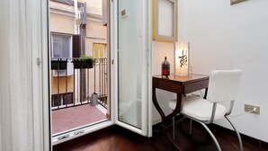 Une pièce avec un bureau en bois, une chaise blanche, une petite table avec une bougie et une vue sur le balcon extérieur.