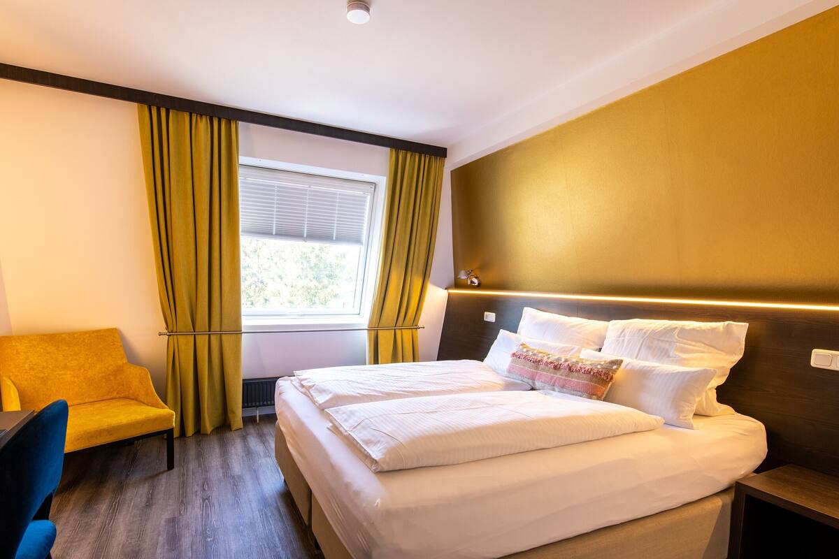 Una habitación de hotel con cama, escritorio, silla y ventana con cortinas.
