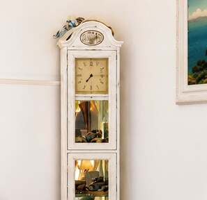 Une grande horloge grand-père blanche, dotée de chiffres romains et d’un balancier, placée contre un mur sobre.