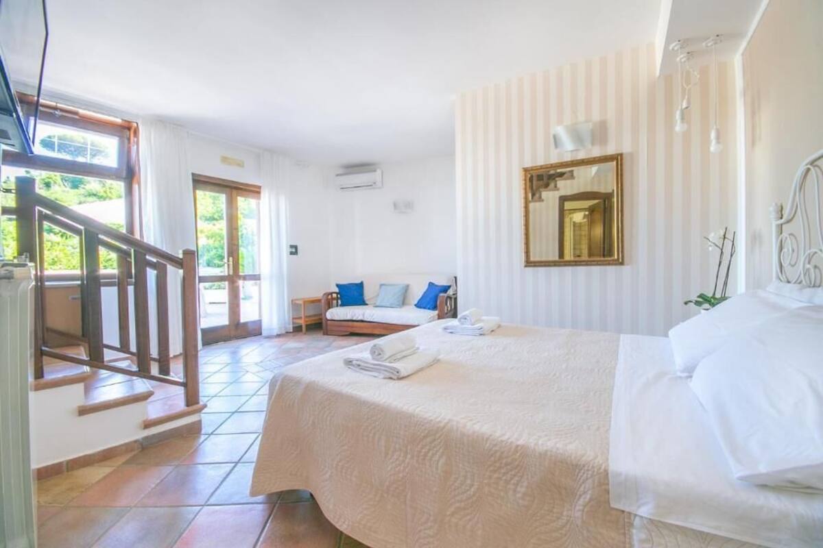 A bedroom with a bed, a sofa, a staircase, and a window.