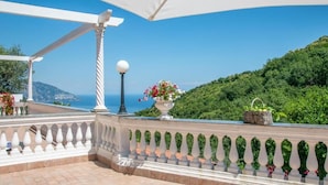Un balcon avec une balustrade blanche, un parasol blanc et une vue sur la mer et la verdure.