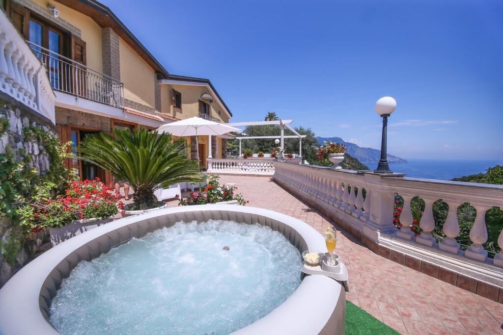 A hot tub with a view of the sea, a balcony with a railing, and a building with a balcony.