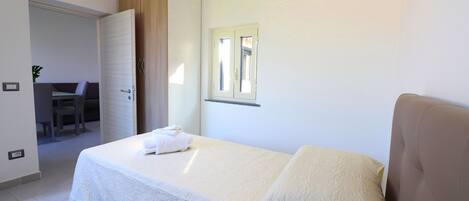 A bedroom with a bed, a bedside table, a window, and a door leading to a bathroom.