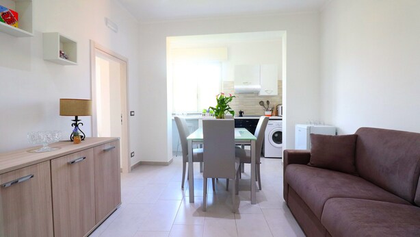 A modern kitchen with white cabinets, a dining table with chairs, and a brown sofa. - Casa Ninà (Sant'Agnello)