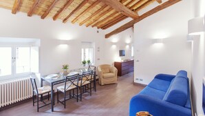 A spacious living area with a high wooden ceiling, a dining table with chairs, a blue sofa, and a white radiator. - Domizio - WR Apartments (Rome)