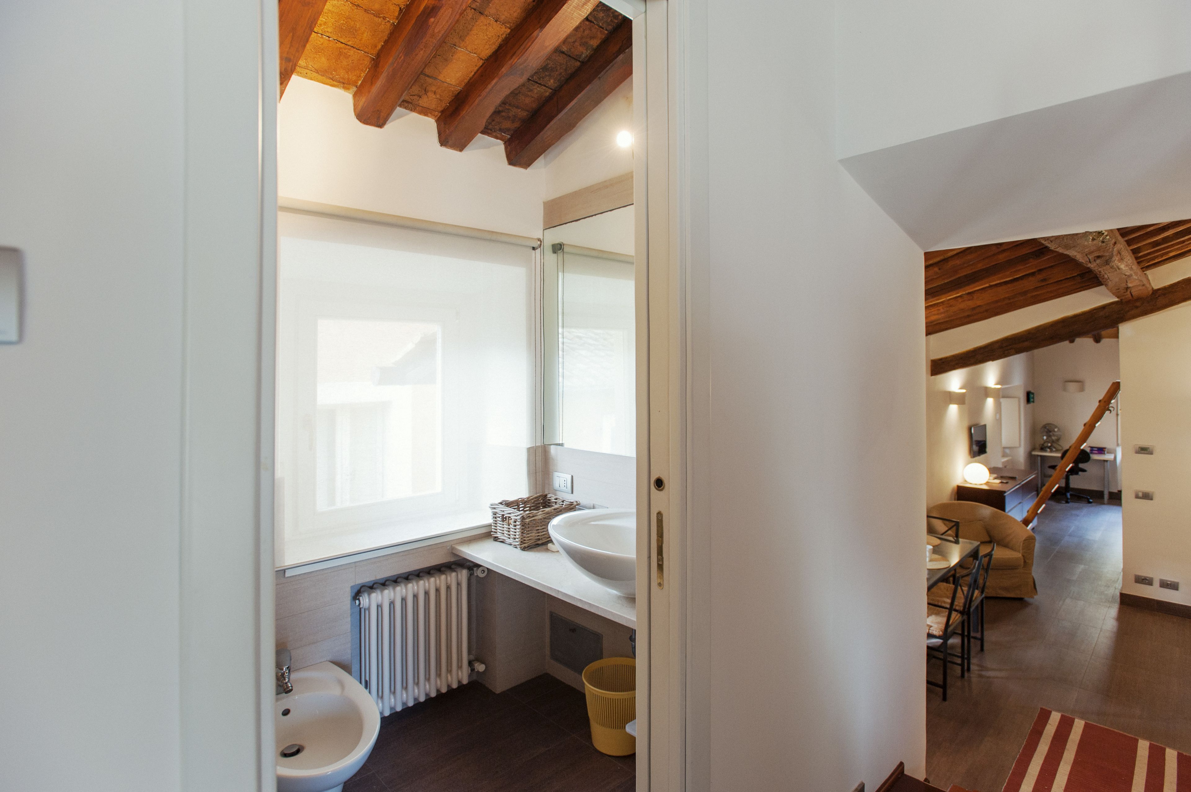 A modern bathroom with a large window, white sink, and wooden ceiling beams.