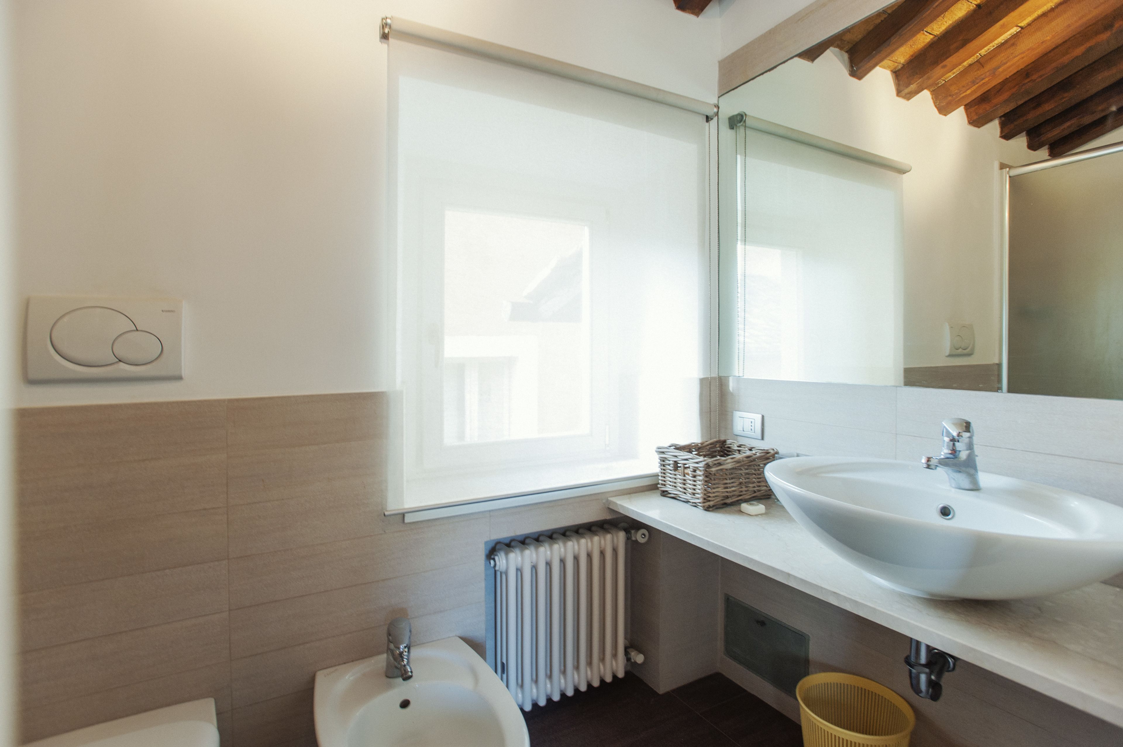 A modern bathroom with a large sink, a mirror, and a window.