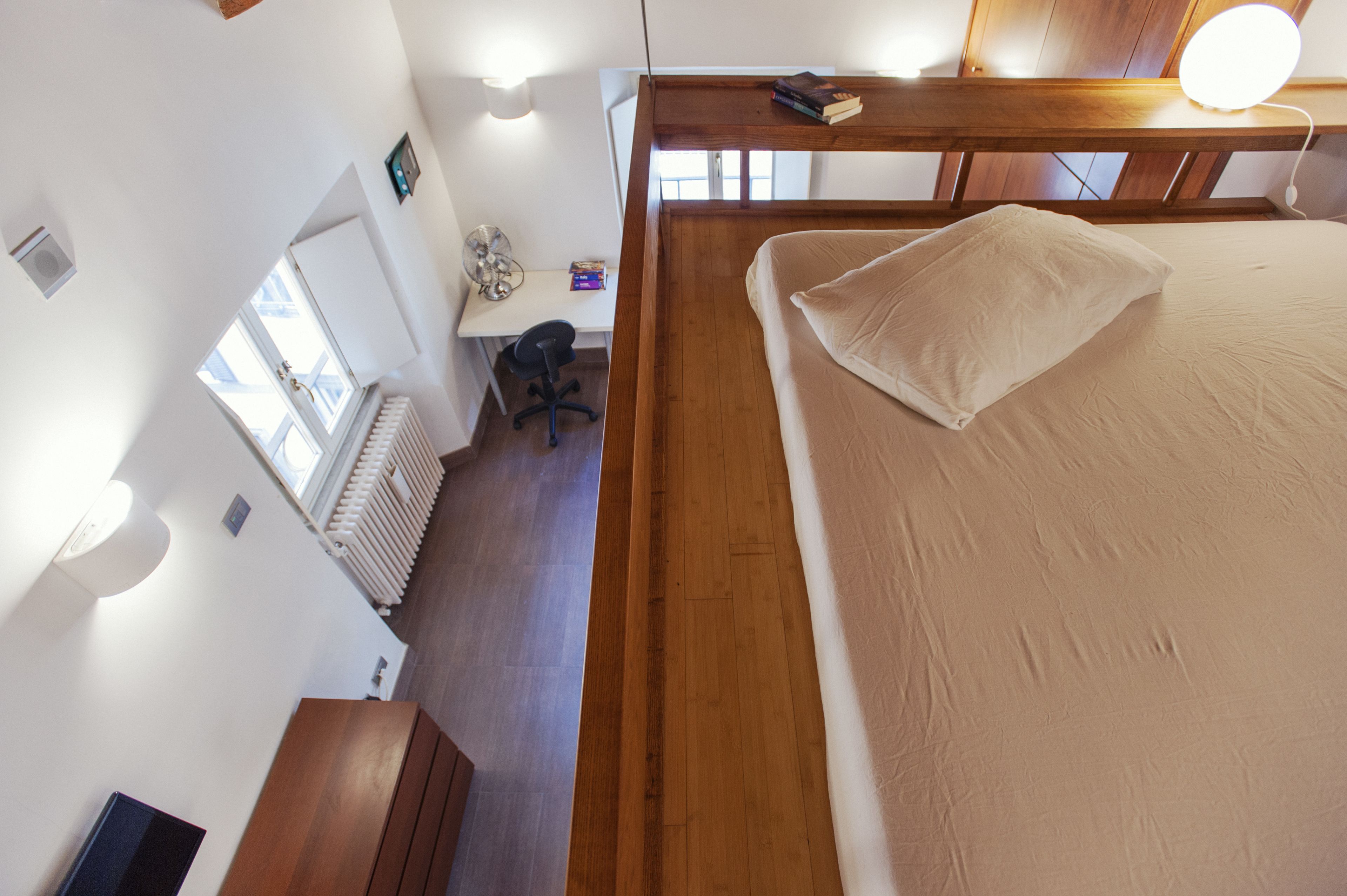 A bedroom with a wooden headboard, a bed with a pillow, a desk with a chair, and a radiator.