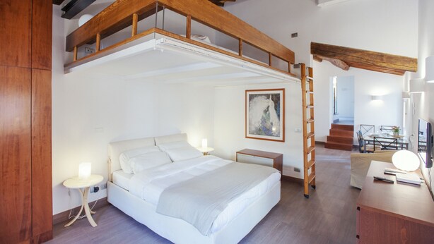 A bedroom with a loft bed, a bedside table, a lamp, a painting, and a desk with a lamp. - Domizio - WR Apartments (Rome)