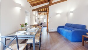 A dining area with a wooden ceiling, a blue sofa, and a kitchen in the background. - Domizio - WR Apartments (Rome)