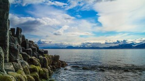Une côte rocheuse bordant un lac paisible, avec des montagnes lointaines se découpant sur un ciel partiellement nuageux.