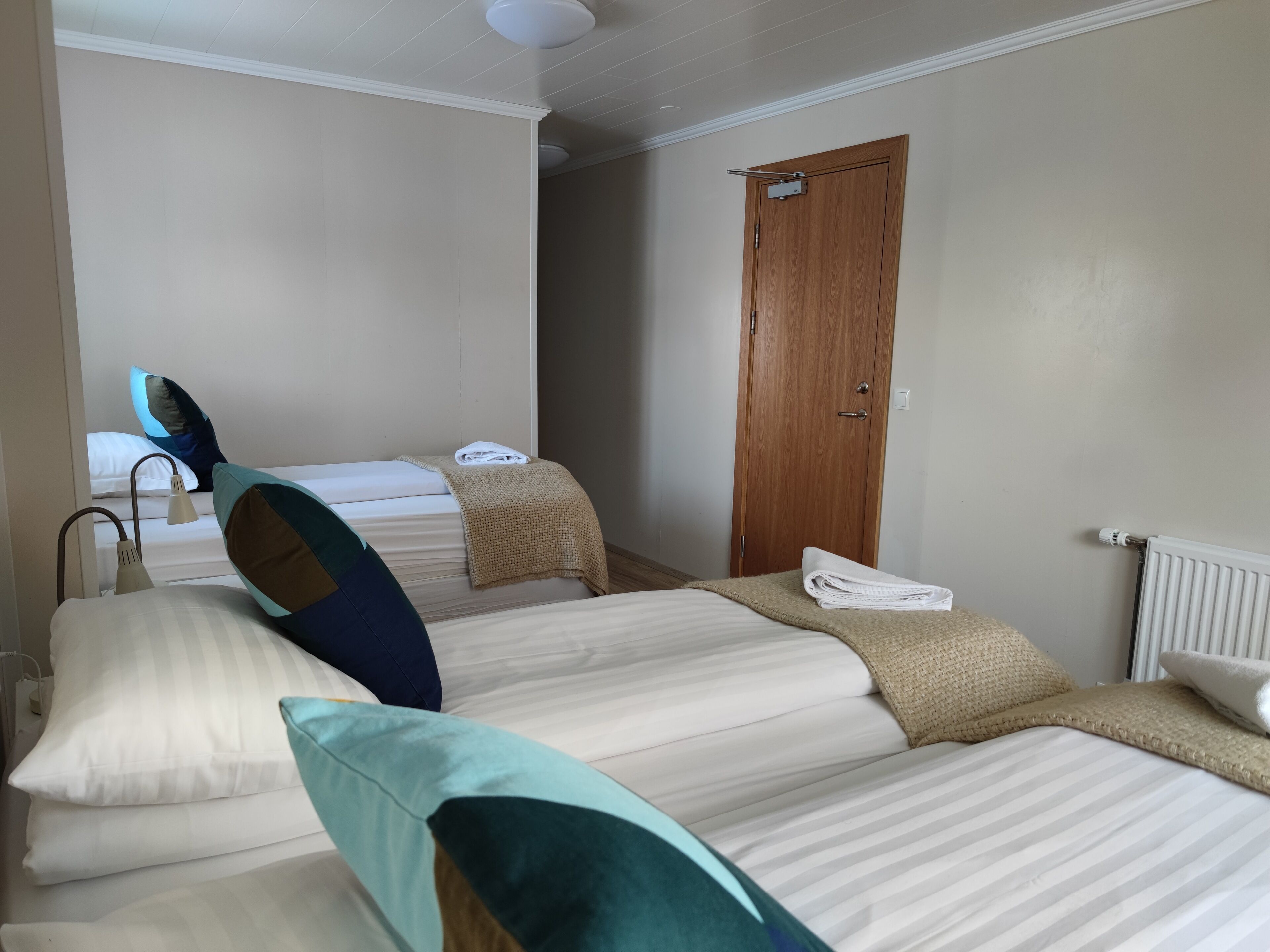 Una habitación de hotel con dos camas, una puerta de madera, un radiador y una mesita de noche con una lámpara.