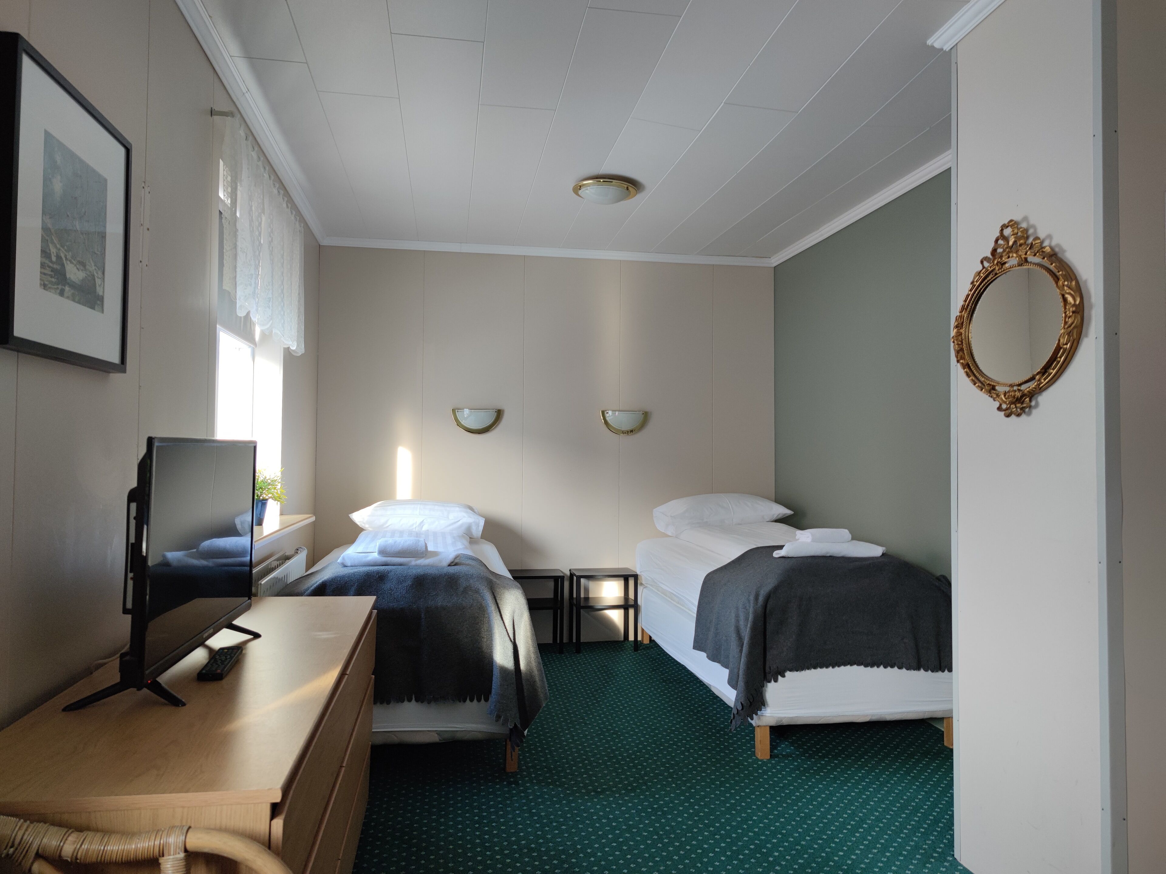 Quarto de hotel com duas camas, uma escrivaninha com computador, um espelho e uma janela com cortinas.