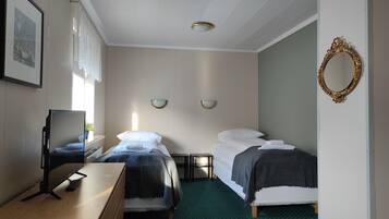 Quarto de hotel com duas camas, uma escrivaninha com computador, um espelho e uma janela com cortinas.