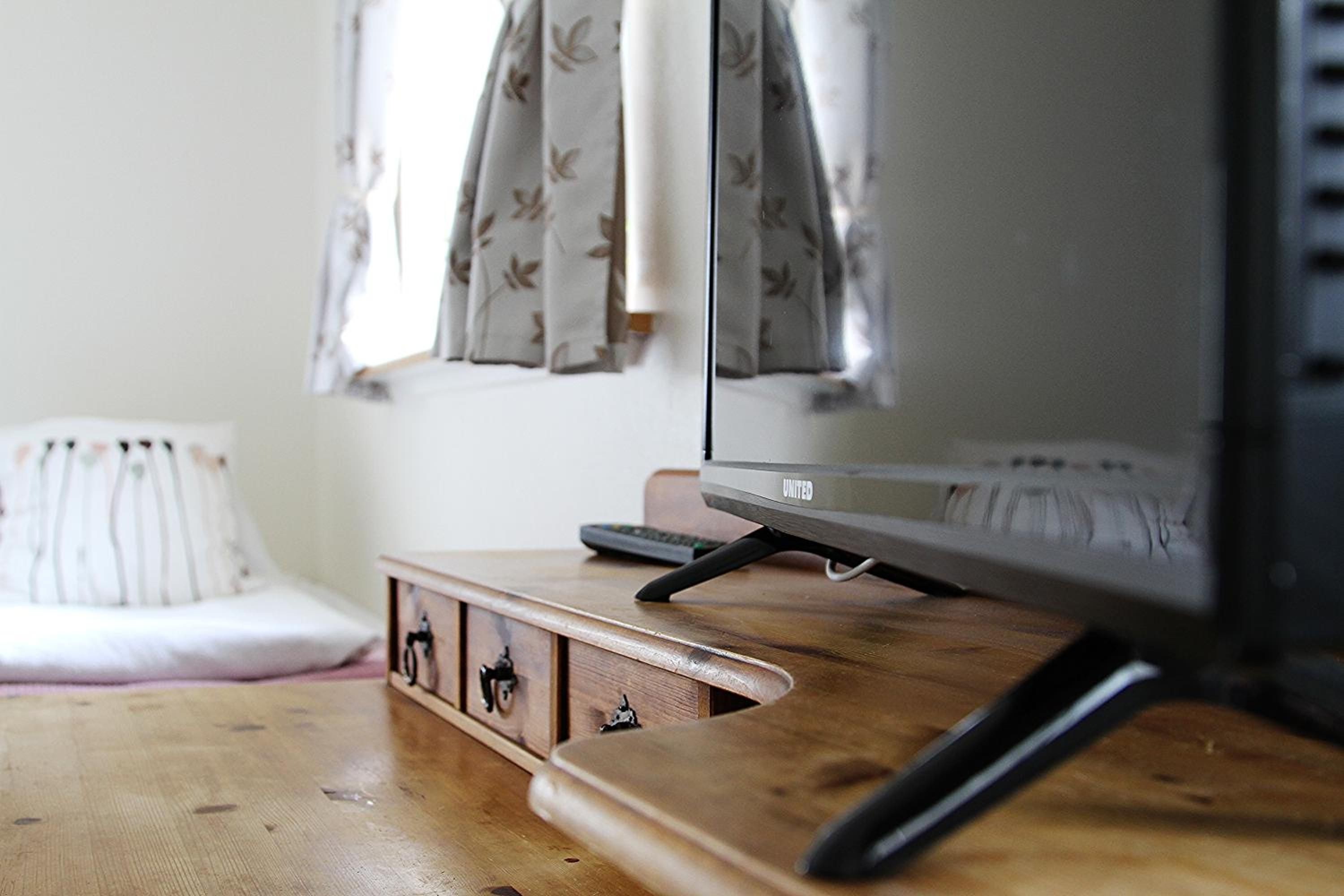 A wooden desk with a television, a remote control, and a small cabinet with drawers.