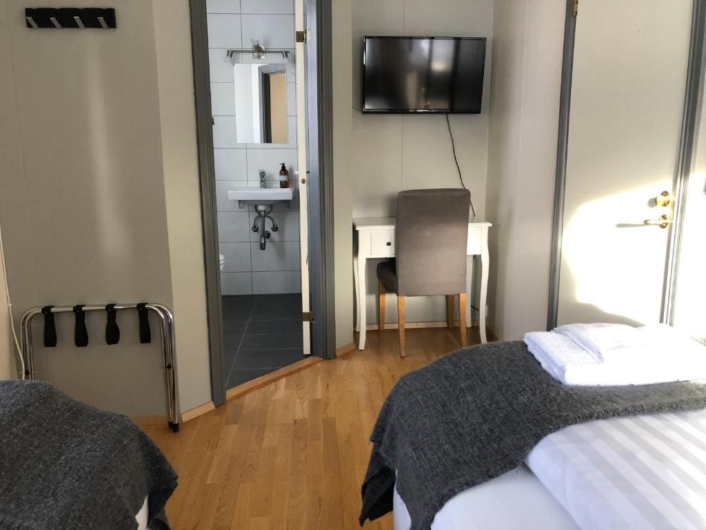 Habitación de hotel con cama, escritorio, silla, televisión y baño visible a través de una puerta abierta.