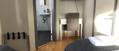 Habitación de hotel con cama, escritorio, silla, televisión y baño visible a través de una puerta abierta.