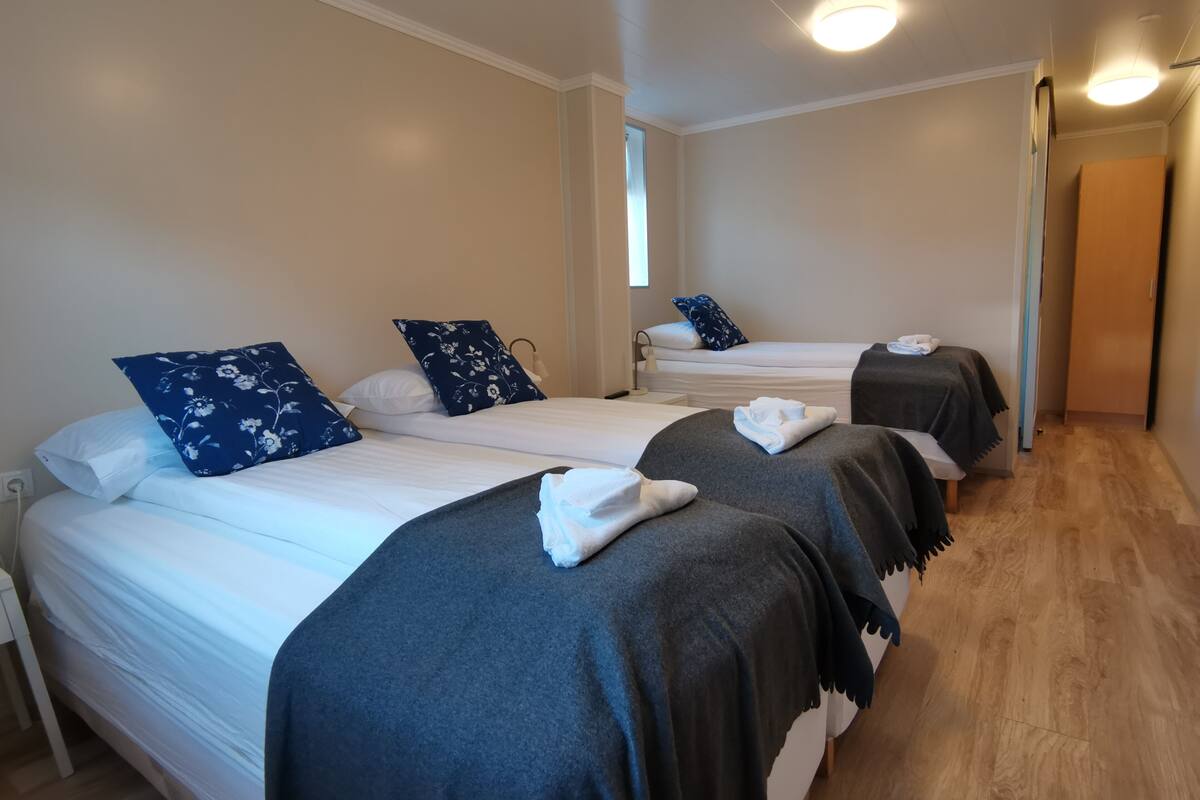 Une chambre d’hôtel avec trois lits, chacun recouvert d’une couverture gris foncé et agrémenté d’oreillers blancs.