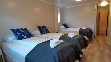 Quarto de hotel com três camas, cada uma com colcha cinza escura e almofadas brancas.