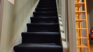Un escalier avec des marches recouvertes de moquette noire, une main courante en bois et une balustrade en métal.